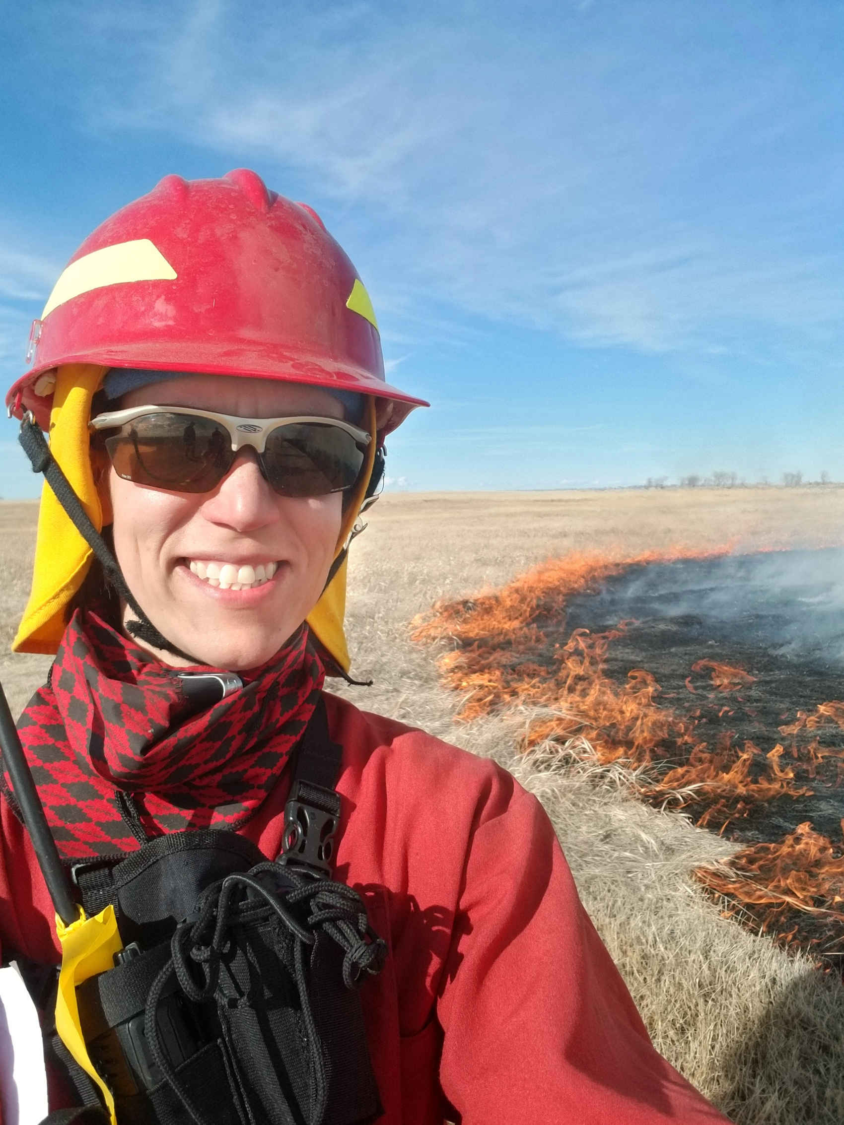 Kerry Hecker wearing a hard hat and protective gear standing in front of burning prairie.
